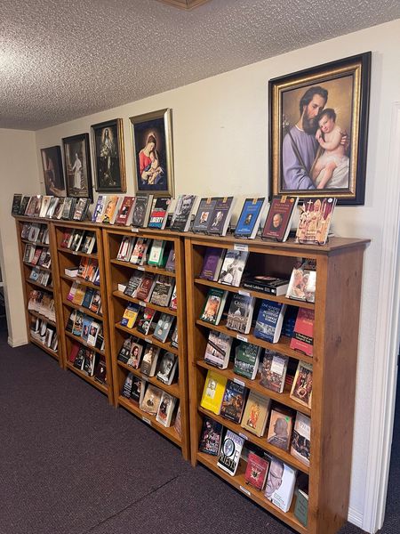Wooden bookshelves filled with Catholic books, with framed paintings of the Madonna and Child and St. Joseph holding the Child Jesus on the wall above.
