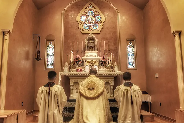 Eucharistic adoration at Our Lady of Fatima Chapel: the priest in a gold humeral veil kneels with two altar servers before the Blessed Sacrament exposed in the monstrance on the high altar.